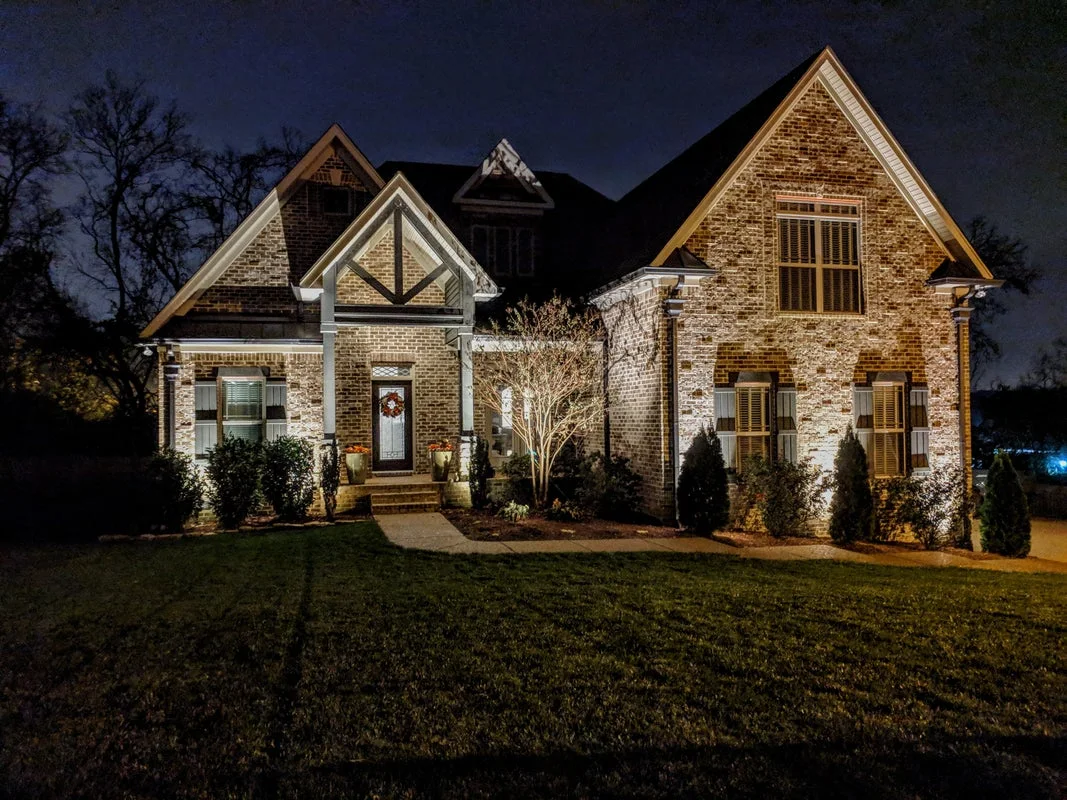Brick home with warm exterior uplighting illuminating its façade and rooflines at night