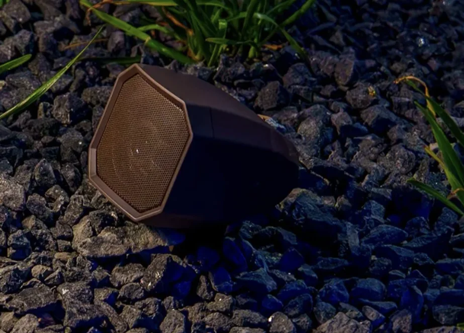Discreet bronze outdoor speaker integrated into a landscaped stone bed