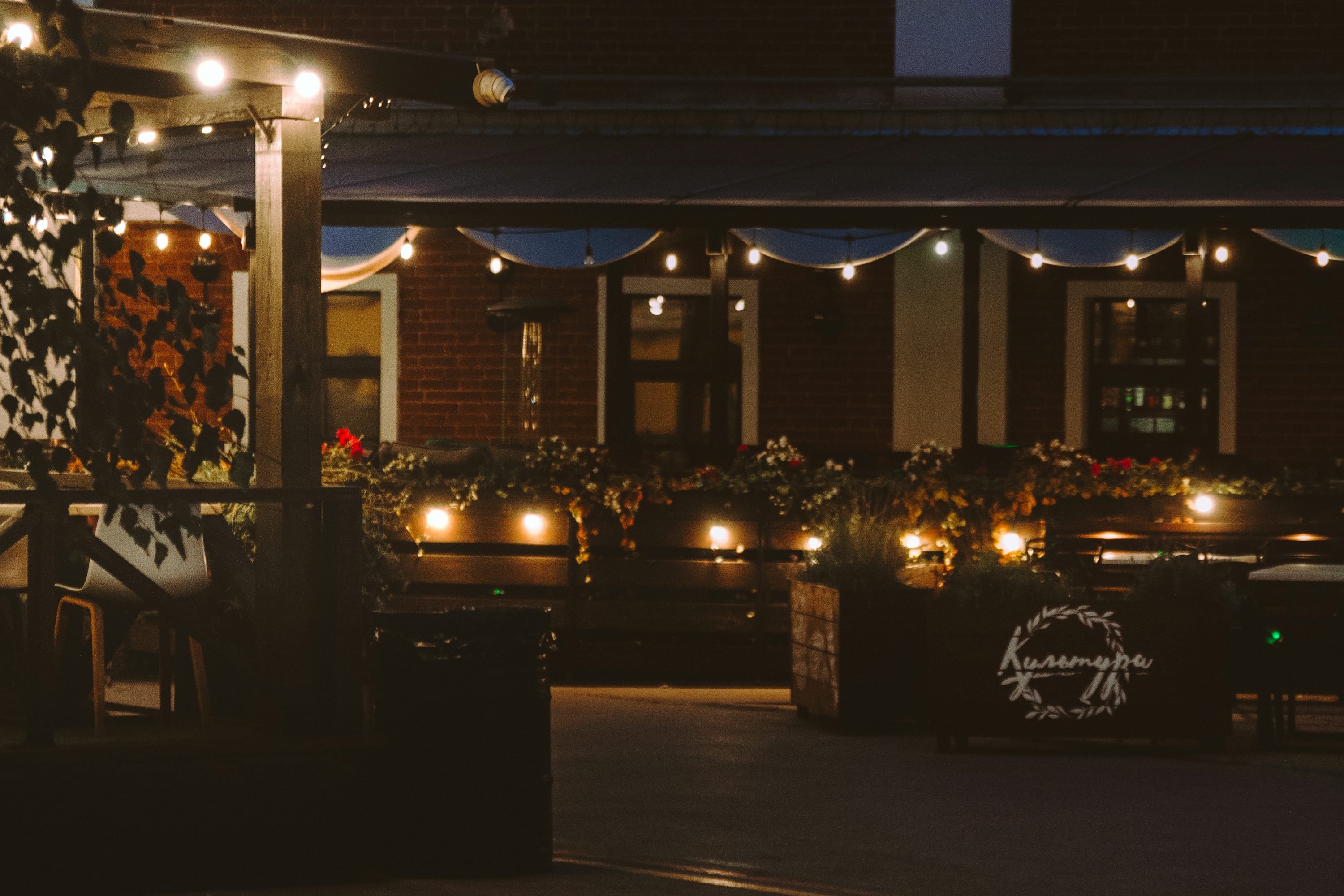 Welcoming outdoor restaurant patio illuminated with warm string lights and landscape lighting at night
